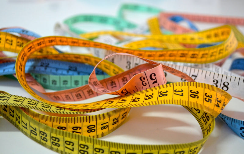 Colorful measuring tapes on a white surface with sewing needles
